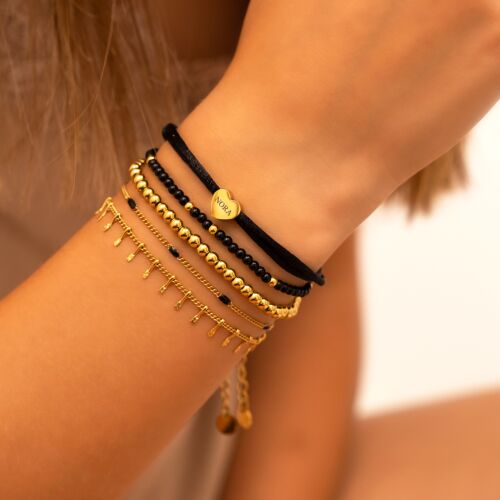 Model draagt gouden armparty met zwart kralen armbandje