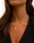 Model draagt gouden necklace layer met dubbele ketting en initialen ketting