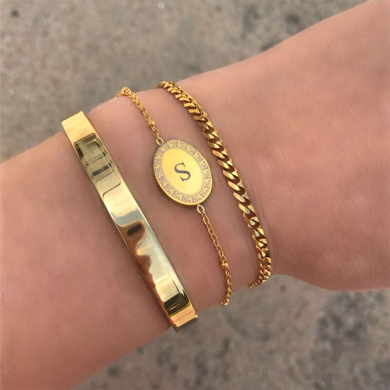 Gouden initial armband om de pols in combinatie met andere gouden