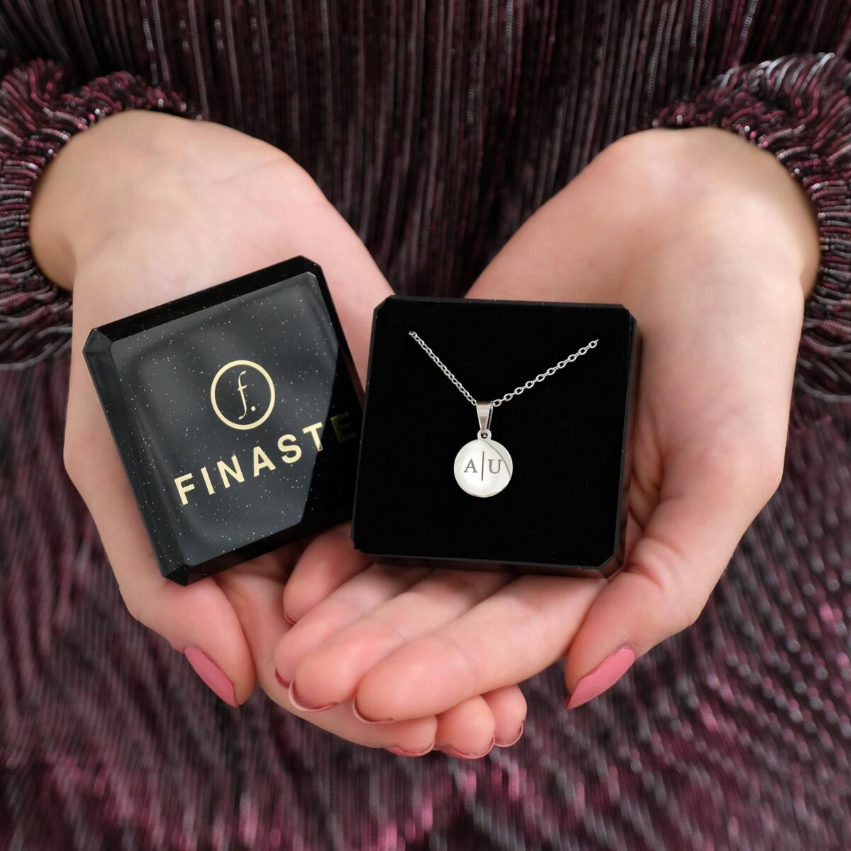 zilveren ketting met initialen op coin in doosje in handen