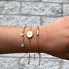 Vrouw draagt initial armband goud samen met schelpjes armband